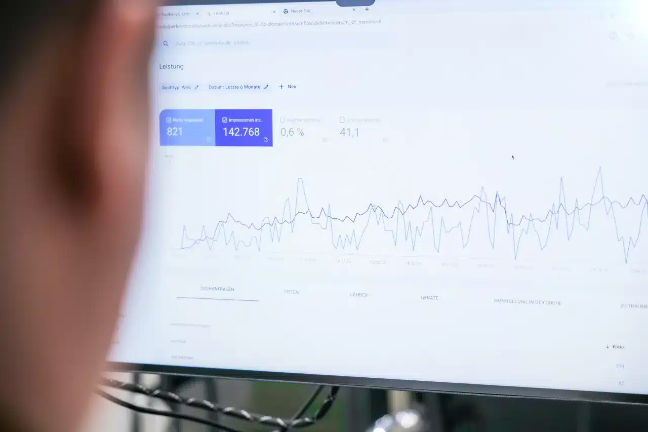 Ein Computermonitor zeigt ein Liniendiagramm mit schwankenden Datenpunkten, das statistische Trends in SEO-Kennzahlen aufzeigt. Der Bildschirm zeigt Zahlen und Prozentsätze, wobei spezifische Details unklar bleiben. Der Vordergrund ist leicht unscharf, wodurch der Fokus auf das Diagramm gerichtet wird.